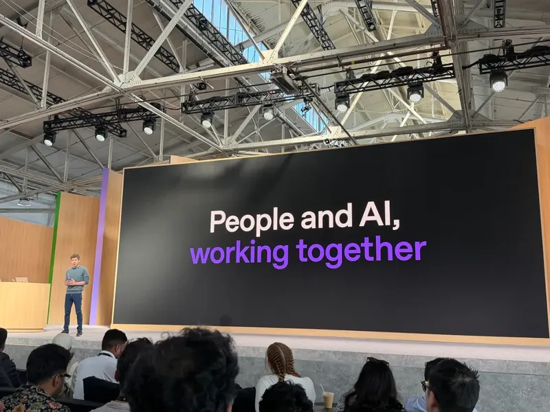 Sam Altman stands on a conference stage before a seated audience, beside a large